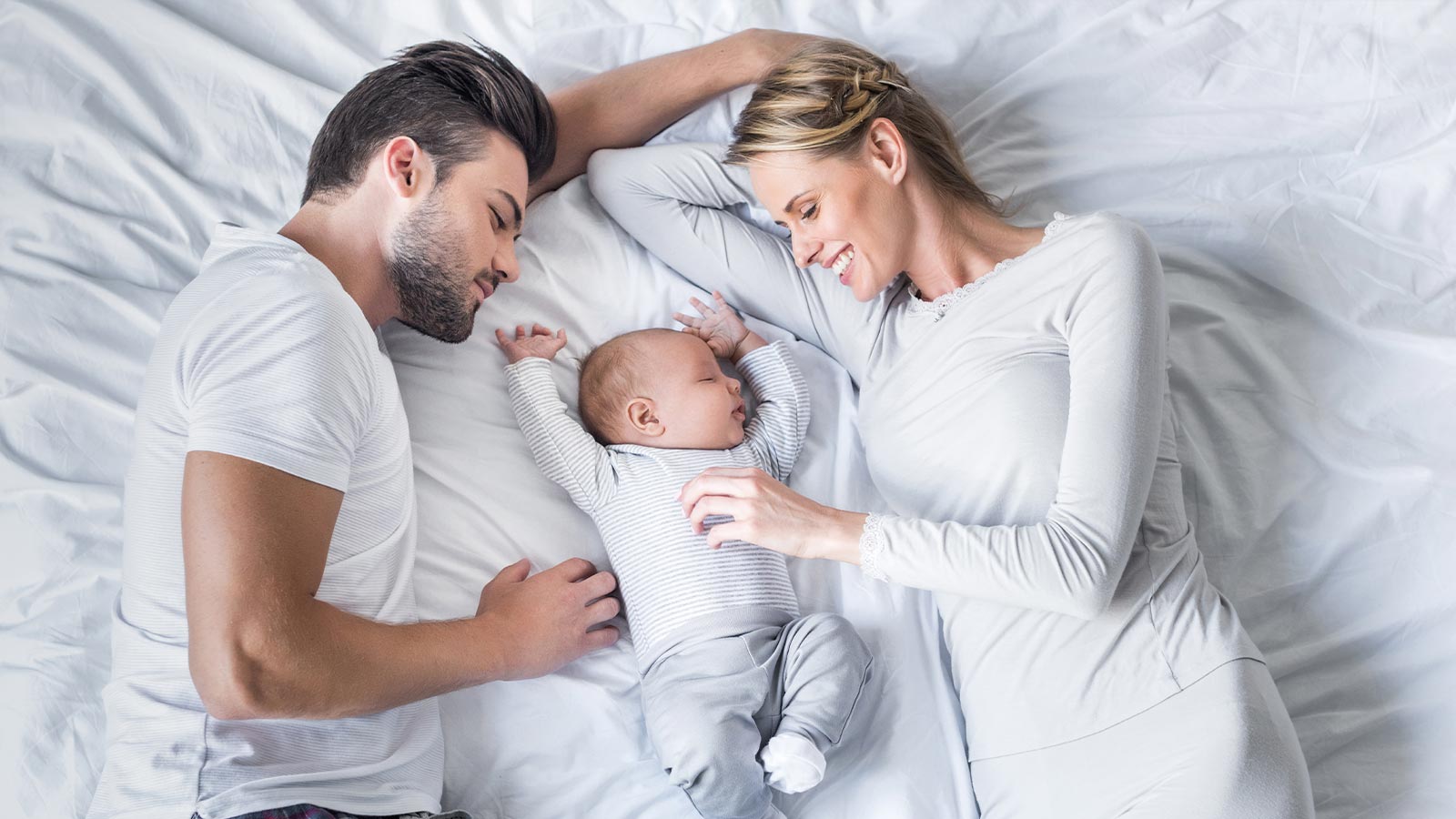 Due genitori coccolano il loro bebè sul letto di una delle camere dell'Hotel Livì a Livigno